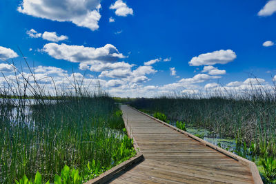 Boardwalk leading to calm lake against sky
