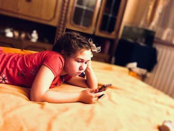 Side view of girl using mobile phone while lying on bed at home