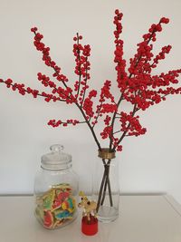 Close-up of red flowers in vase on table against wall