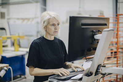 Serious mature woman using computer while standing in industry