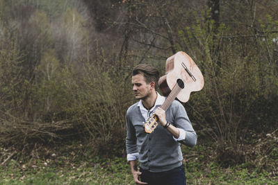 Young man with guitar standing in forest