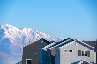 Houses and snowcapped mountains against clear blue sky
