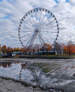 Ferris wheel by lake against cloudy sky