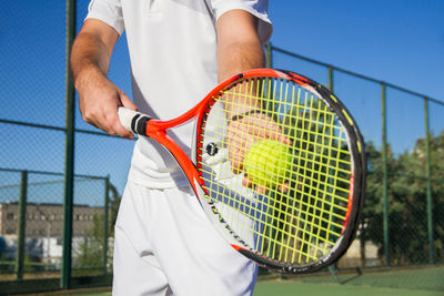 Midsection of man playing tennis against blue sky in court