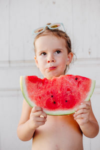 Shirtless girl eating watermelon against wall