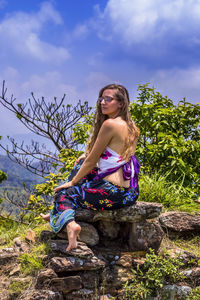 Young woman looking away while sitting on rocks