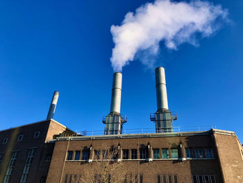 Low angle view of smoke emitting from chimney against blue sky
