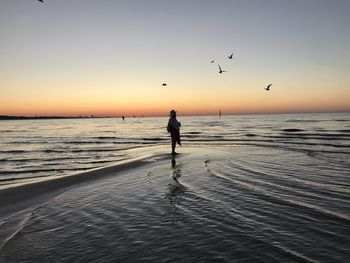 Silhouette woman standing on beach against sky during sunset