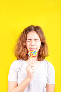 Cute girl holding lollipop against yellow background