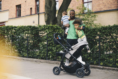 Father with children standing by baby stroller on sidewalk in city