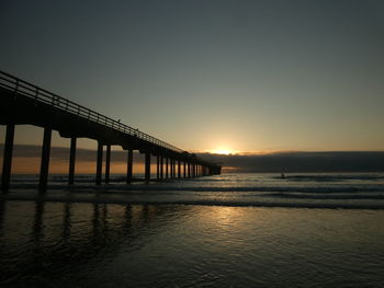 Silhouette pier over sea against clear sky during sunset