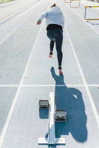 Back view of unrecognizable sportswoman beginning to run fast from starting blocks during track and field workout on stadium