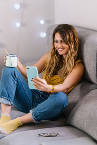 Young woman using phone while sitting on sofa