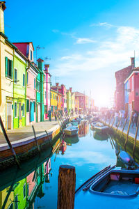 Boats moored in canal by buildings against sky