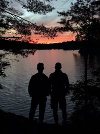 Silhouette men standing on lake against sky during sunset