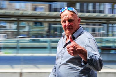 Portrait of mature man showing thumbs up sign against buildings in city