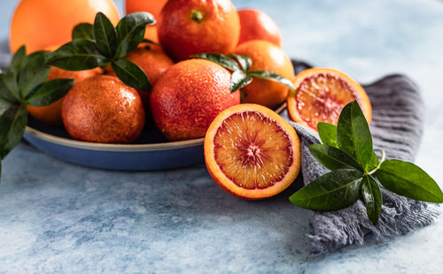 Ripe juicy sicilian blood oranges with leaves on ceramic plate, blue concrete background.