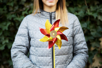 Midsection of young woman holding pinwheel toy while standing against plants at park