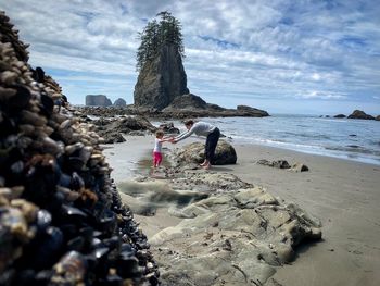 Mother with daughter standing at beach against sky