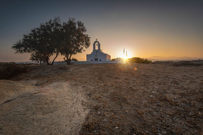 Lighthouse amidst trees and buildings against sky at sunset