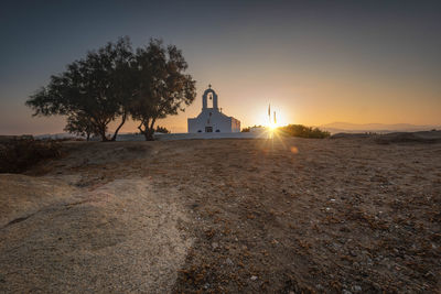 Greek church amidst trees and buildings against sky at sunset