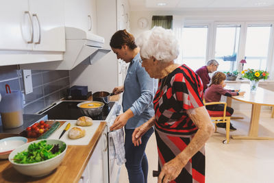 Side view of senior woman and daughter cooking food in kitchen