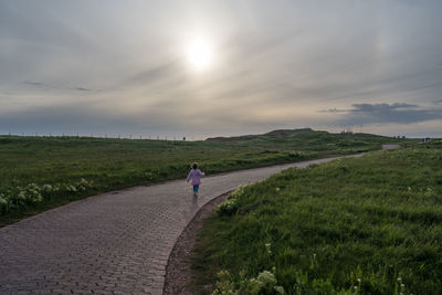 Rear view of girl walking on footpath against sky