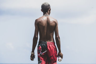 Rear view of shirtless man standing against sky