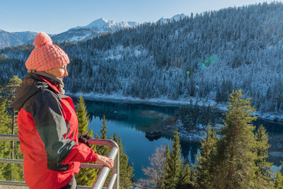 Woman looking at view while standing on observation point by lake against mountain during winter