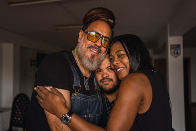 Smiling adult multiracial friends in casual clothes embracing while standing together and looking at camera