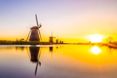 Traditional windmills by lake against sky during sunset