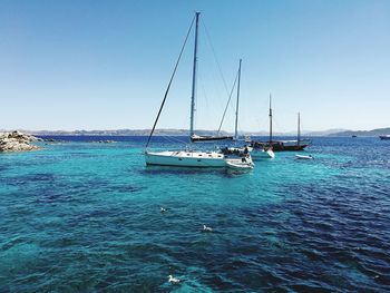 Boats sailing in sea against clear blue sky