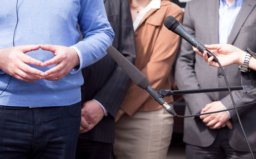 Cropped hand of woman holding microphone in front of people