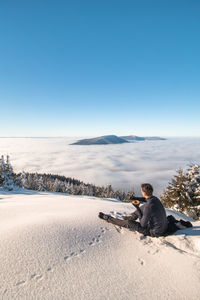 Rear view of man sitting on snow covered landscape