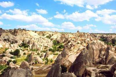 Rock formations on field against cloudy sky during sunny day