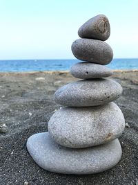 Stack of stones on sand at beach against sky