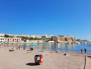 People on beach against clear blue sky