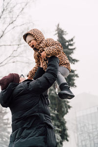 Low angle view of father picking daughter mid air during winter