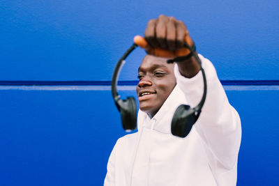 Young man holding headphones against blue wall