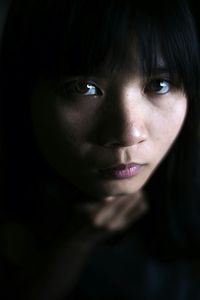 Close-up portrait of young woman against black background