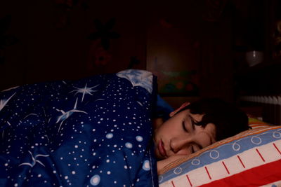 A caucasian boy sleeps in the bed of his bedroom covered by a quilt with a spatial motif