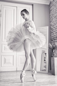 Charming ballerina poses showing her legs in the room in front of the mirror in pointes and tutu