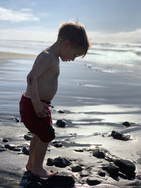 Full length of boy standing at beach against sky