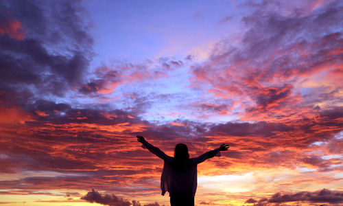 Rear view of girl with arms outstretched standing against dramatic sky