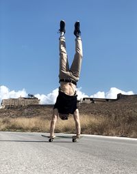 Full length of man doing handstand on skateboard against blue sky