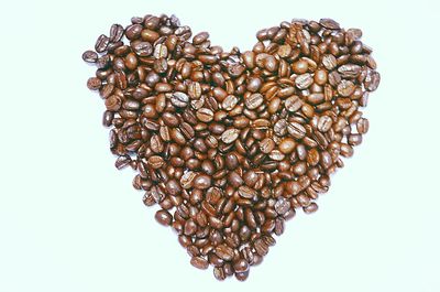 Close-up of coffee beans arranged in heart shape over white background