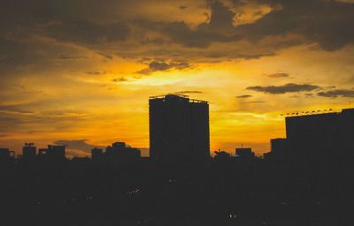 Silhouette of city against cloudy sky during sunset