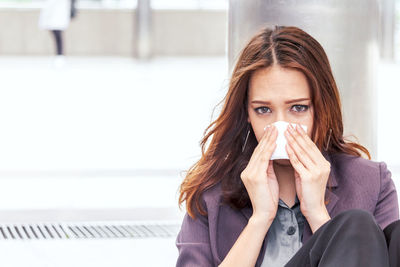 Portrait of young woman covering nose with handkerchief on walkway