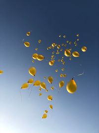 Low angle view of yellow balloons flying against blue sky