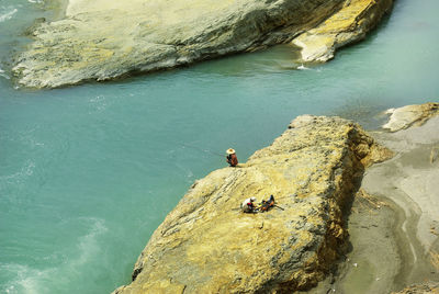 High angle view of people fishing while sitting on rock by sea